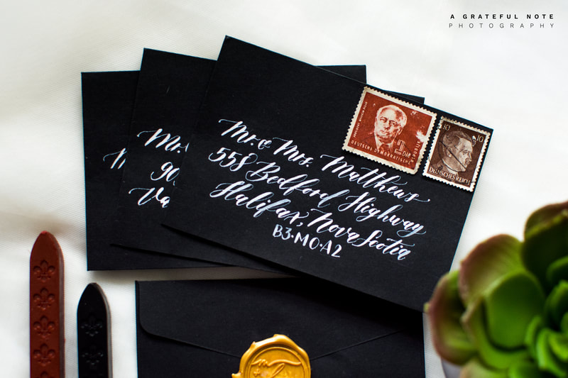 Custom White Calligraphy Addressing on Black Envelopes with Gold Wax Seal and Vintage Stamps.