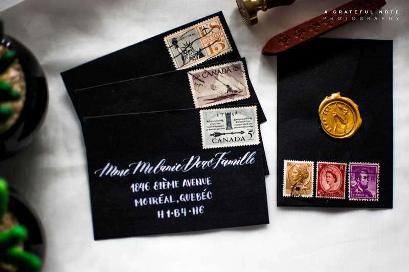 Custom White Calligraphy Addressing on Black Envelopes with Gold Wax Seal and Vintage Stamps Flatlay.